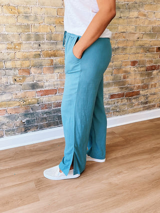 Person wearing teal pants and white shoes standing against a brick wall.