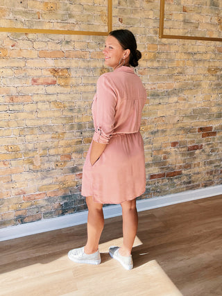Woman in a pink dress standing against a brick wall.