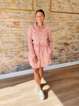 Person wearing a pink dress standing in front of a brick wall.