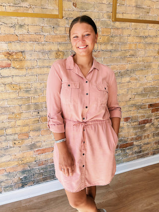 Woman wearing a pink dress standing against a brick wall.