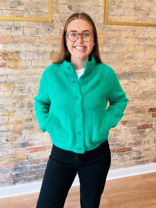 Person wearing a green sweater standing against a brick wall.