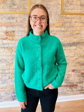 Person wearing a green jacket standing against a brick wall.