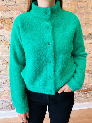 Green cardigan worn by a person against a brick wall.