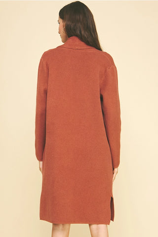 Person wearing a long rust-colored coat on a beige background
