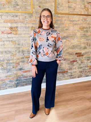 Woman wearing the Mirna Sweater with abstract floral print and puff sleeves, paired with navy pants.