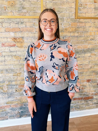 Woman smiling while wearing the Mirna Sweater with peach, navy, and grey floral design.