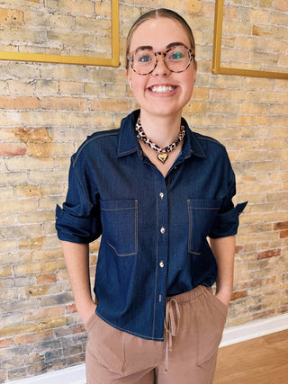Person wearing a blue shirt and brown pants standing against a brick wall.